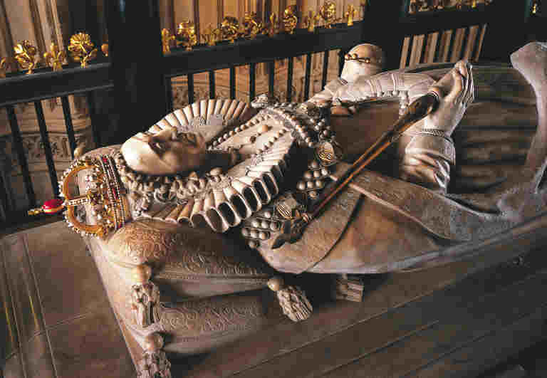 White marble recumbent effigy of Mary Queen of Scots, wearing a gold crown and holding a sceptre and orb