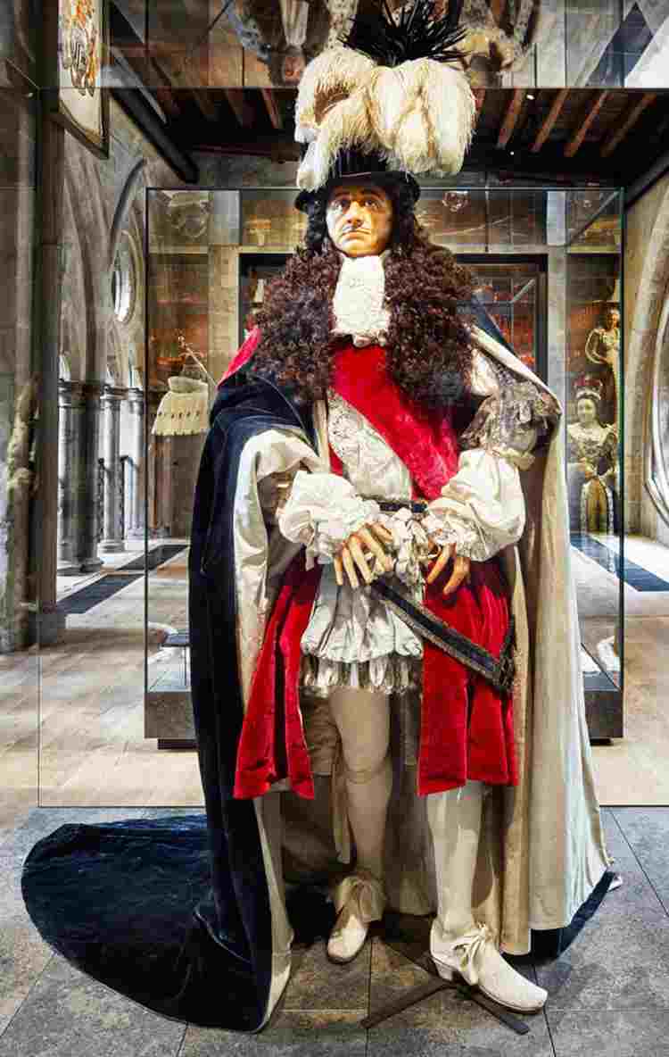 Wax effigy of Charles II with brown curly hair, black velvet cloak, hat with feathers in it and red sash