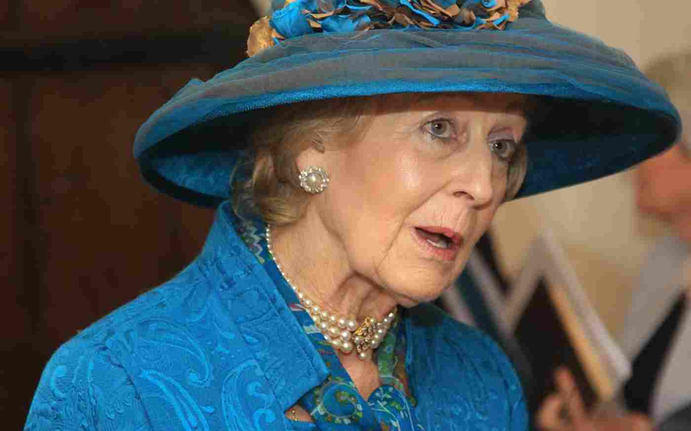 Princess Alexandra wearing a blue hat with blue and gold flowers, a blue dress and pearl necklace