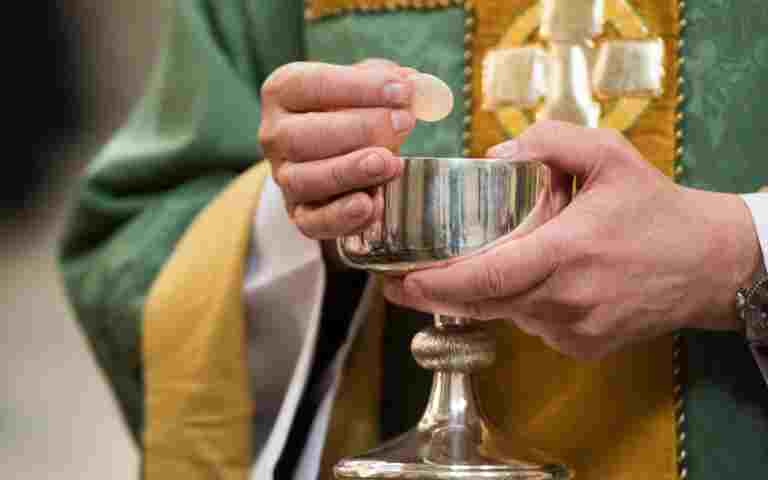 A priest holds a communion wafer and a silver chalice