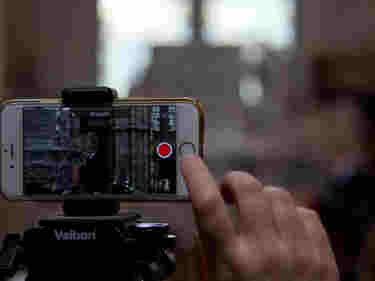 Photograph of a mobile phone recording a video of the Abbey with a person's finger pressing the button to start it