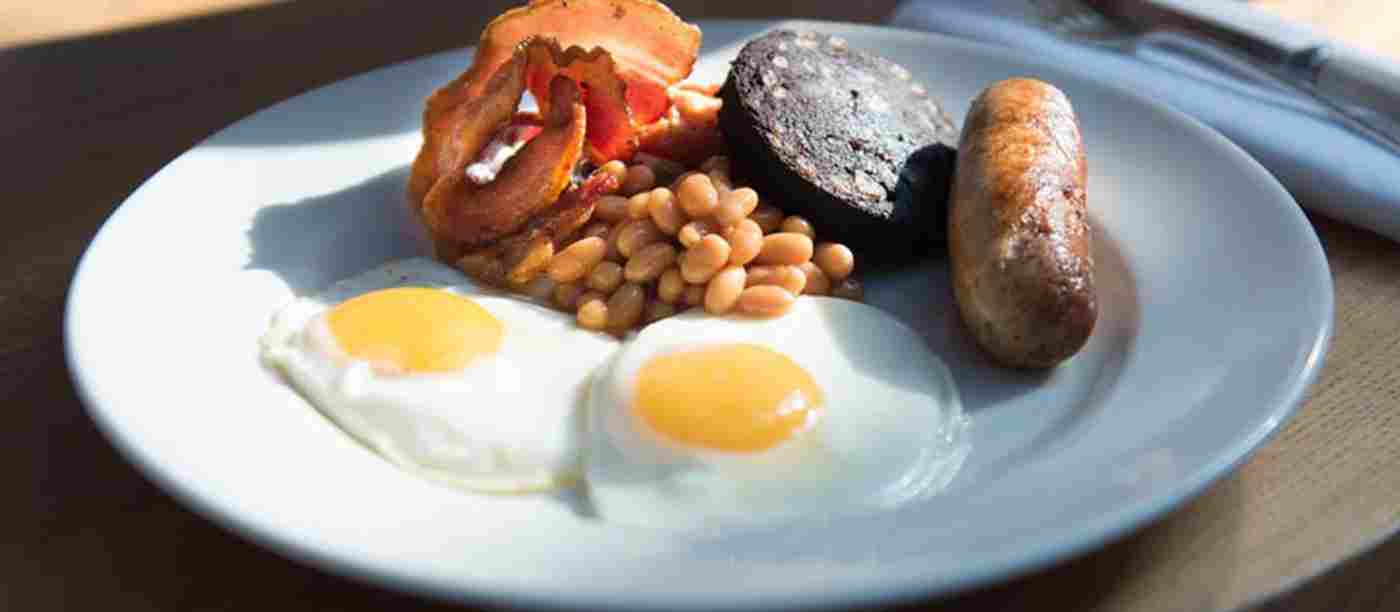 A plate of Full English breakfast at the Cellarium Cafe: Streaky bacon, Cumberland sausage, black pudding, two fried egg and baked beans