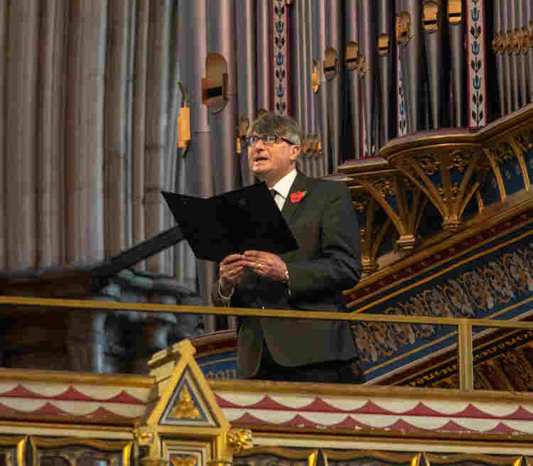 Photograph of Simon Armitage standing on the organ loft, reading his poem, in Westminster Abbey