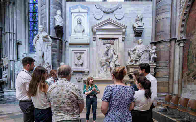 Photograph of member of staff delivering a tour to a group of visitors standing within Poets' Corner in Westminster Abbey