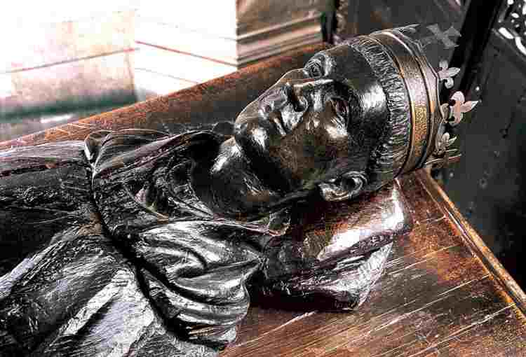 Modern carved head of tomb effigy of Henry V wearing a crown, his head resting on a pillow