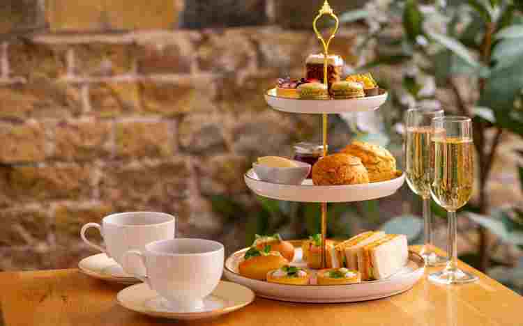 Two empty teacups next to a selection of cakes and pastries with two glasses of prosecco