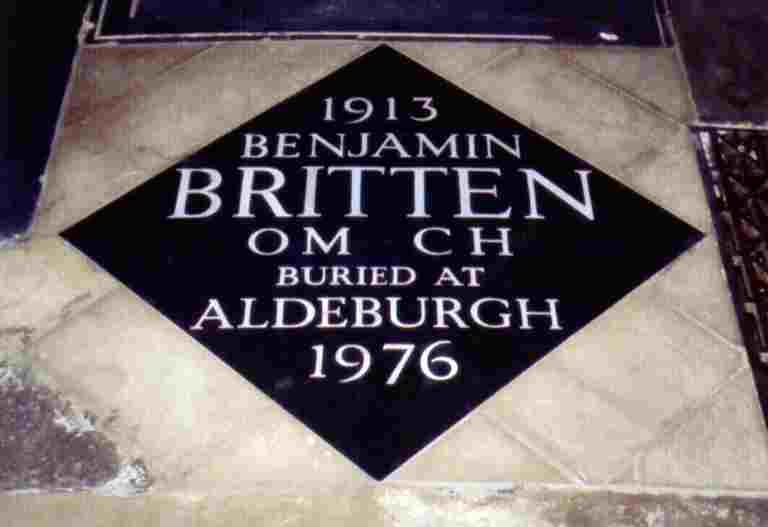 Black, diamond-shaped memorial stone engraved with '1913 BENJAMIN BRITTEN OM CH BURIED AT ALDEBURGH 1976'