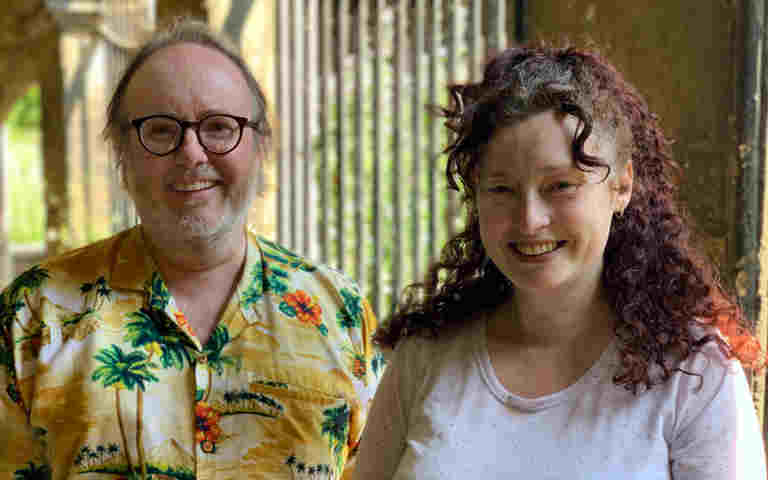 Photograph of Ewen, a white male wearing glasses and a patterned shirt, with Gemma, a white woman with red hair and a pale t-shirt, standing in the cloisters at Westminster Abbey