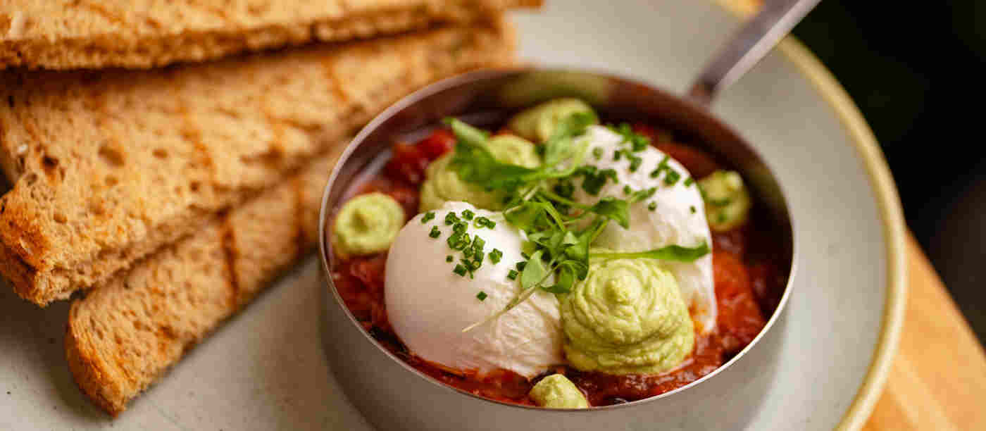 Poached eggs with smashed avocado in a red salsa next to toast