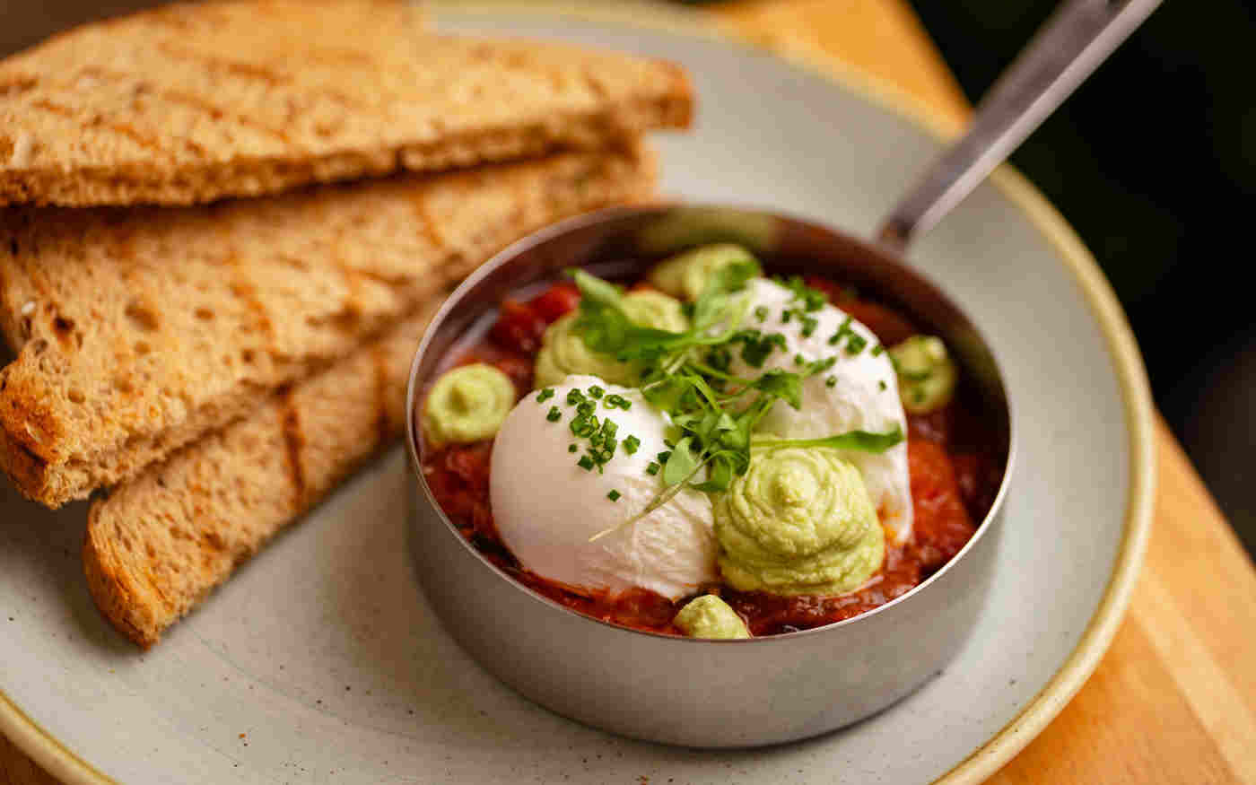 Poached eggs with smashed avocado in a red salsa next to toast