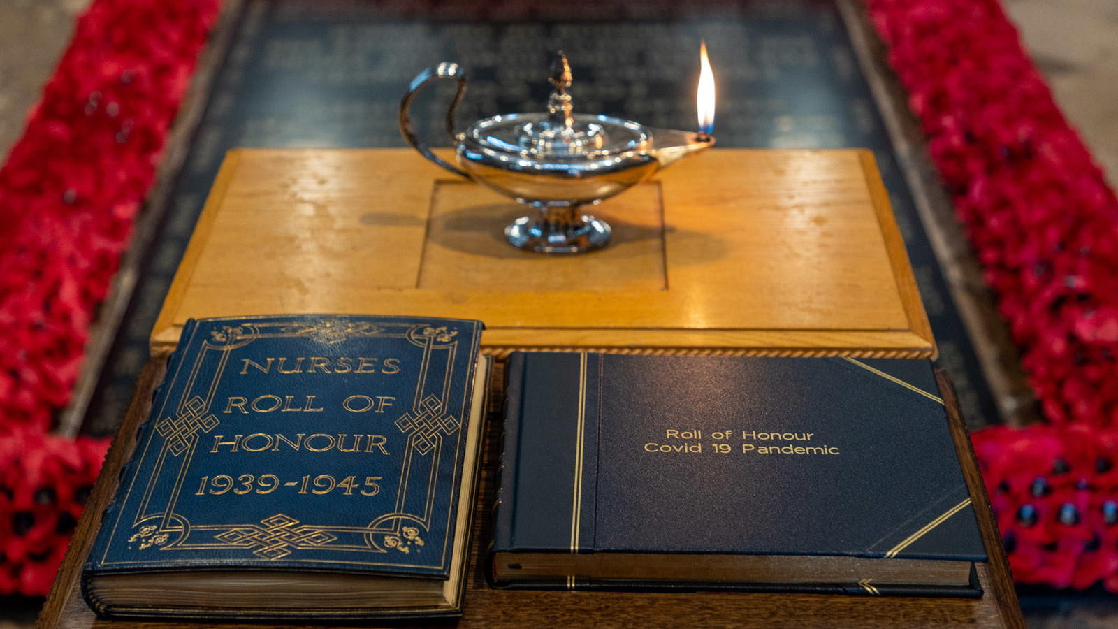 Rolls of Honour in front of a lamp that has a flame at the spout