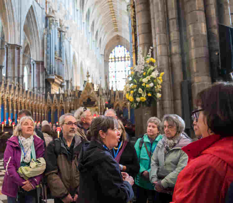 Photograph of a group of visitors listening and looking engaged with their surroundings with a Blue Badge Guide as part of a tour, standing within the crossing of Westminster Abbey