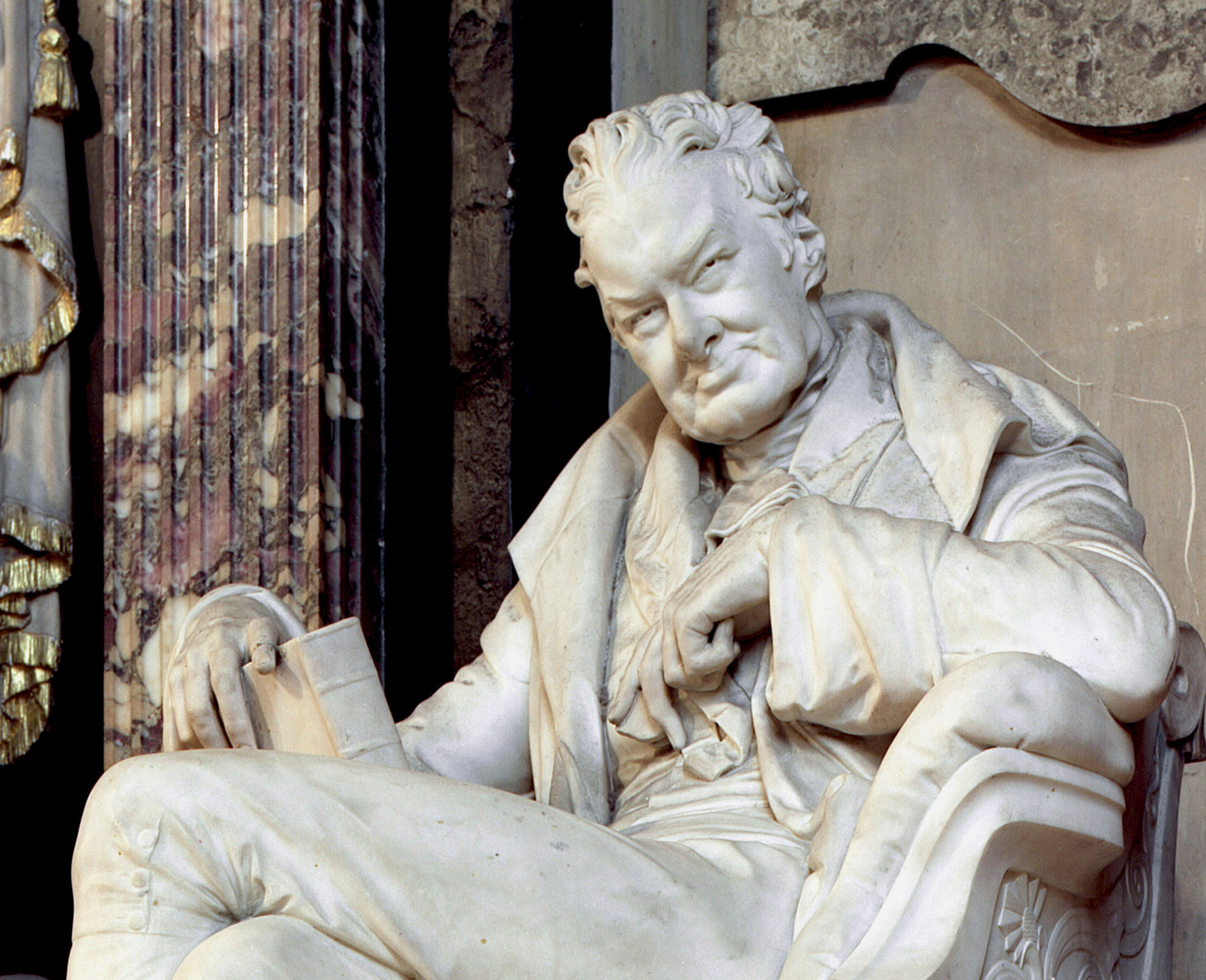 Photograph of statue memorial to William Wilberforce, showing a seating man looking down and holding a book