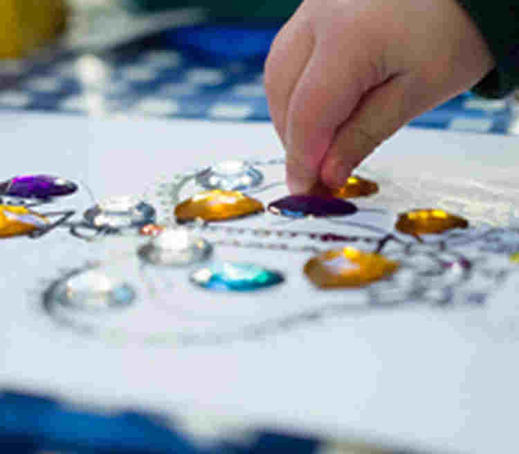 Photograph of a child sticking jewels onto paper, advertising the online collection of Abbey at home craft activities