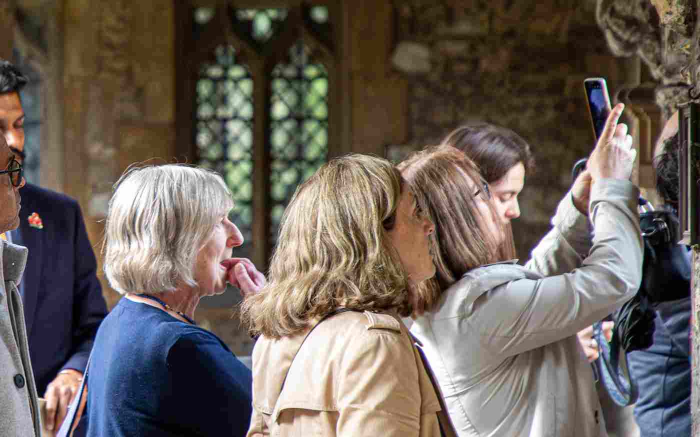 Photograph of a group of visitors looking at medieval stone, with one taking a photograph on their phone, within Westminster Abbey