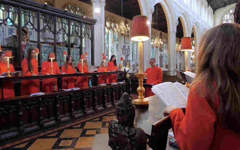 Photograph focusing on one side of St Margaret's Choristers, wearing red robes, singing in St Margaret's Church, Westminster Abbey