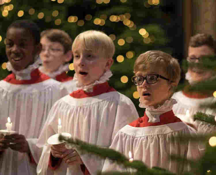 Photograph of Westminster Abbey choristers holding candles singing at Christmas, with a Christmas tree in the bottom right hand corner,