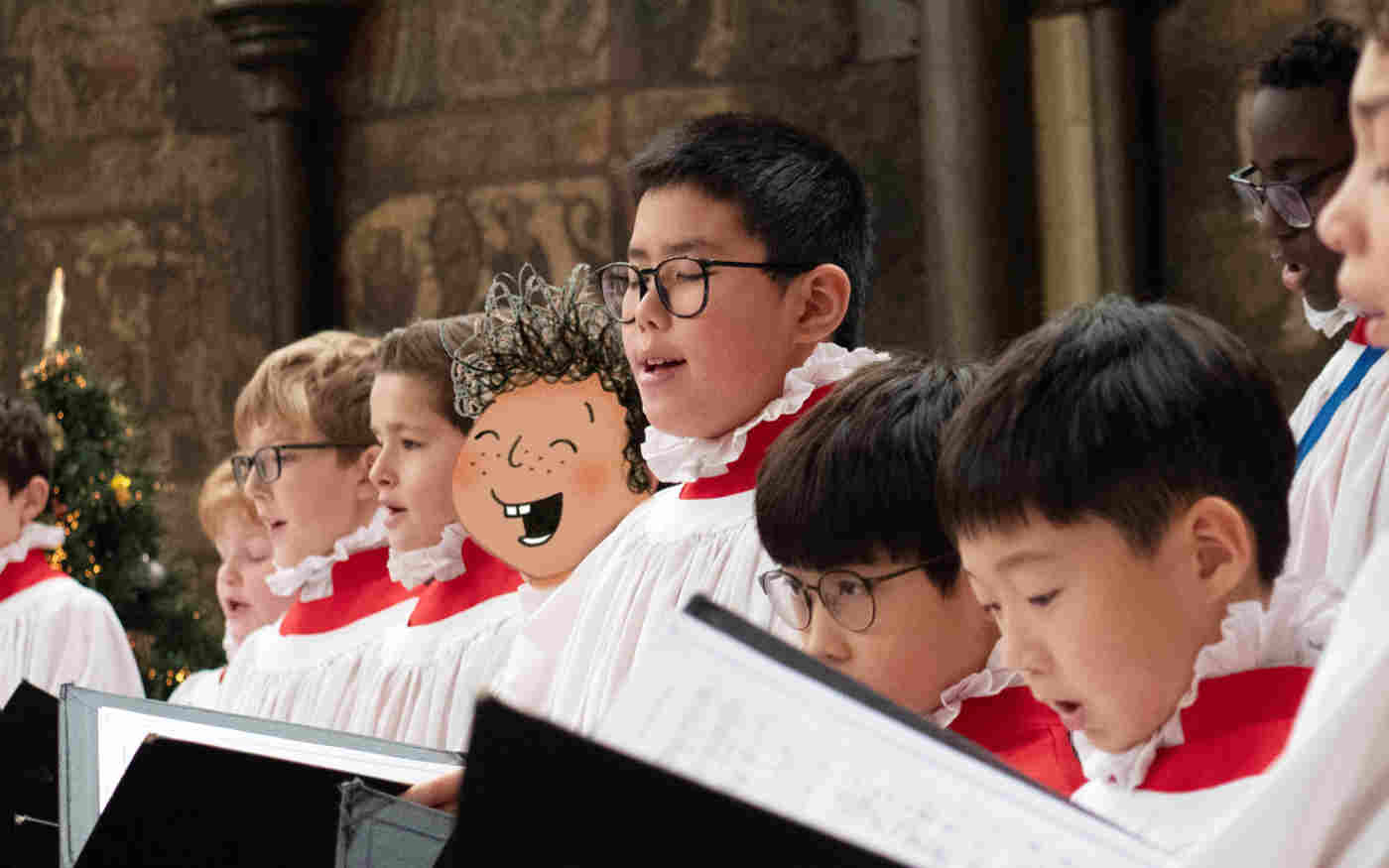 Photograph of singing choristers dressed in white robes with a red collar holding black folders containing sheet music. An illustration of a boy is included as in part of the choir.