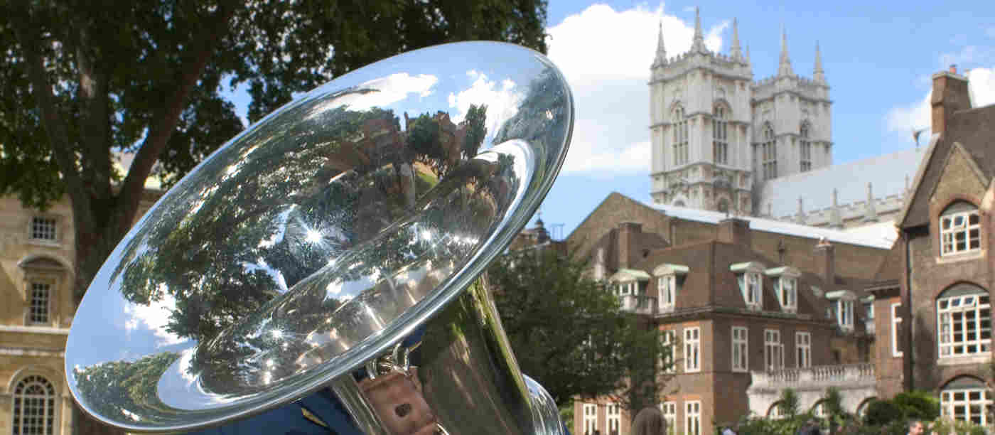 Photograph of top of tuba, part of a brass band, with building around College Garden including Westminster Abbey in the background