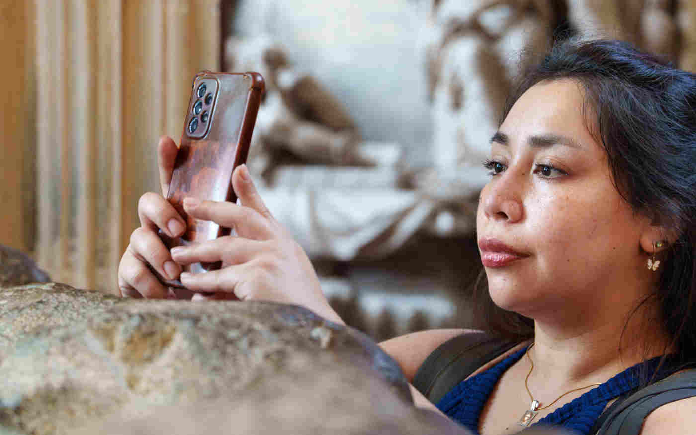 Photograph of member of the public standing next to a stone memorial holding up their phone to take a photograph
