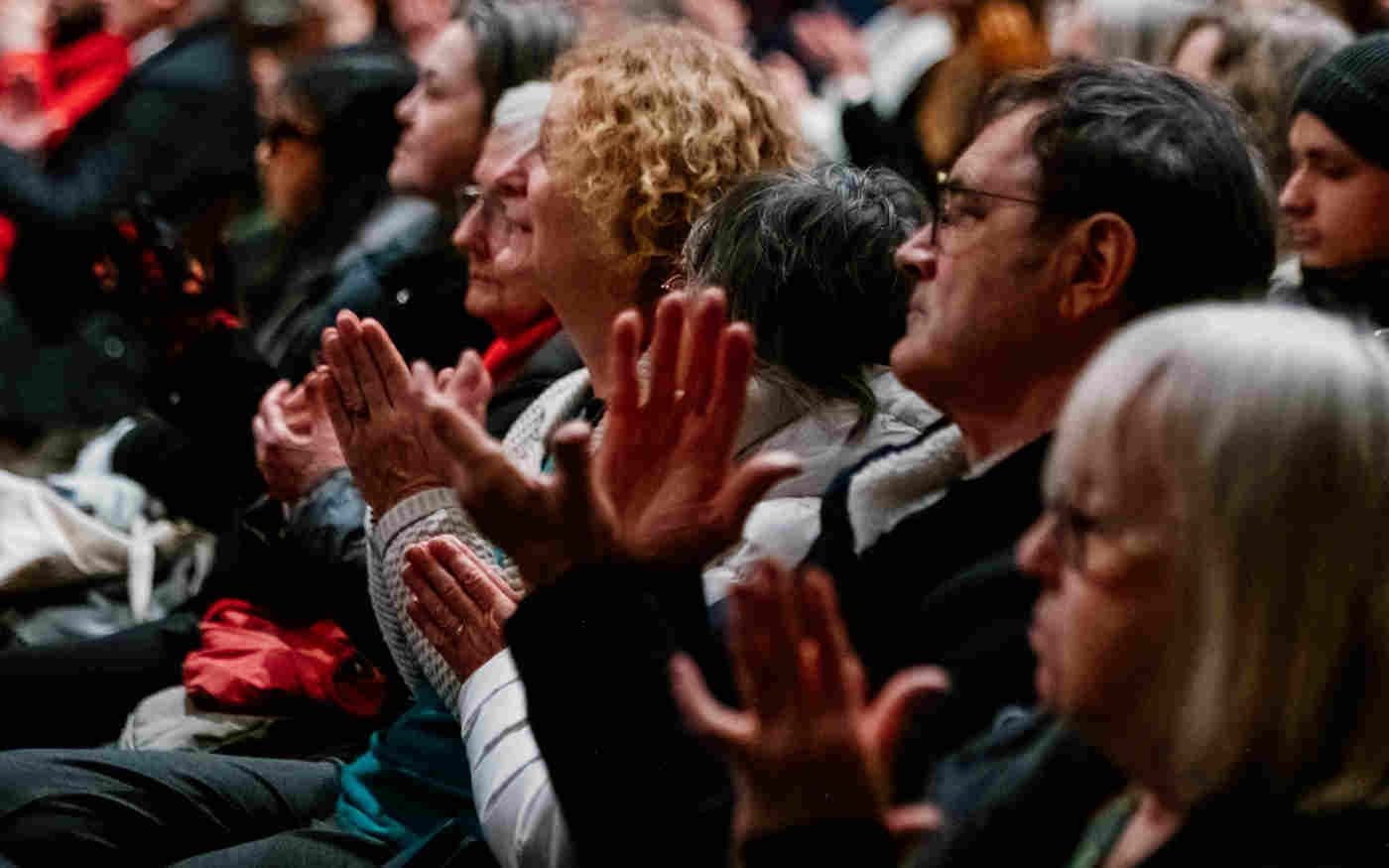 Close-up photograph of a handful of visitors seated and clapping listening to a talk