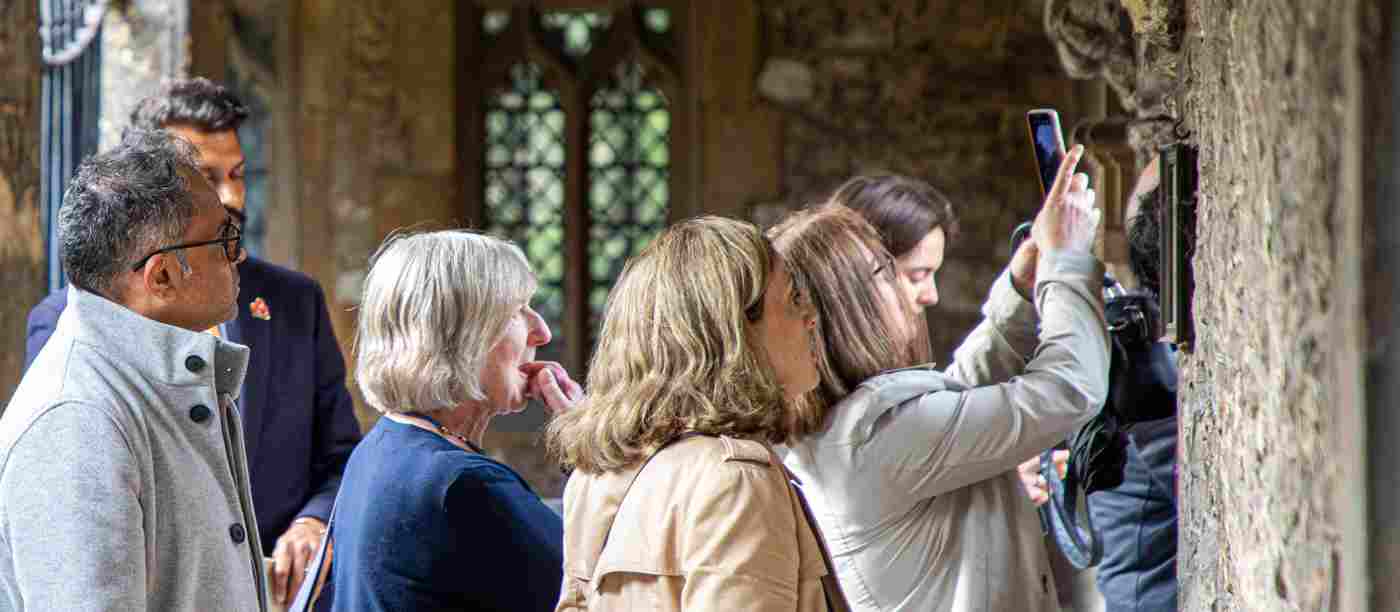 Photograph of people on a tour group looking and taking photographs near a stone wall in Westminster Abbey