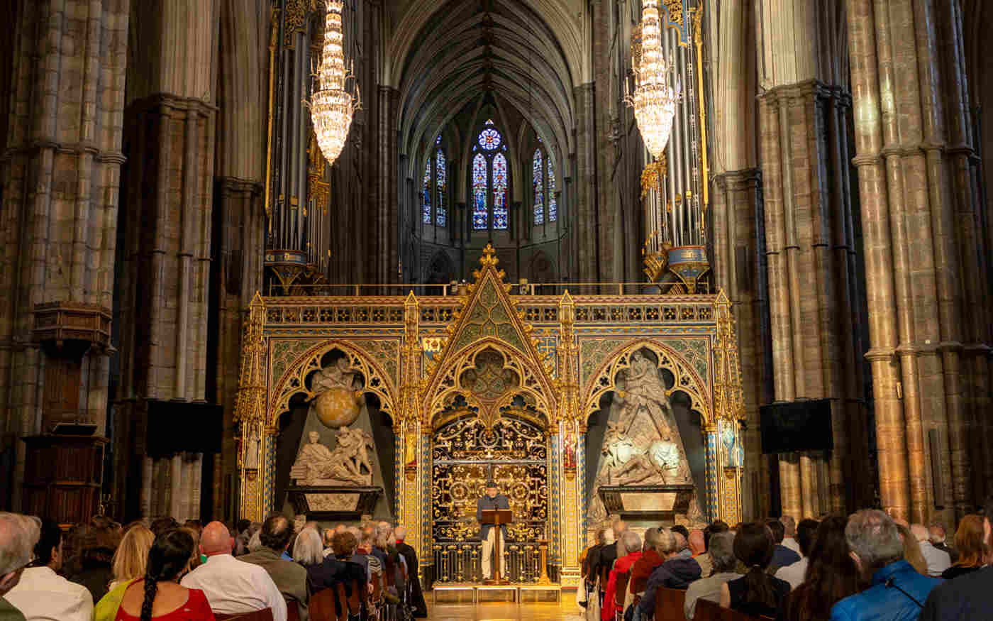 Photograph of a the back of a seated talk with a speaker standing in front of the nave screen within Westminster Abbey