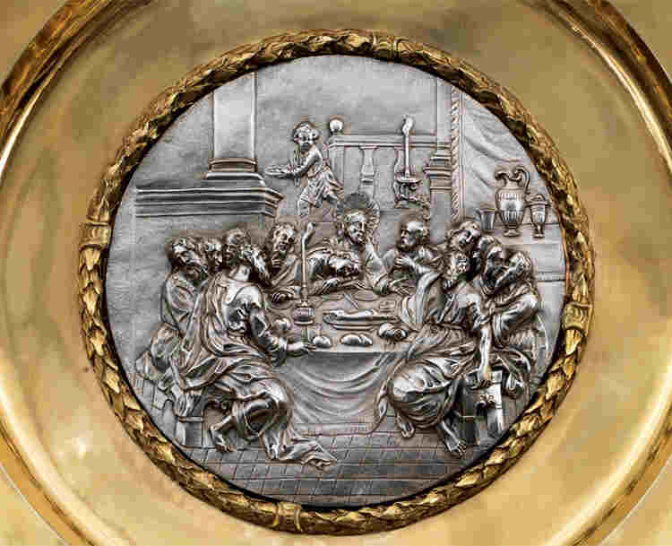 Photograph of golden collection plate with image of the Last Supper, representing the Bible in Christian art