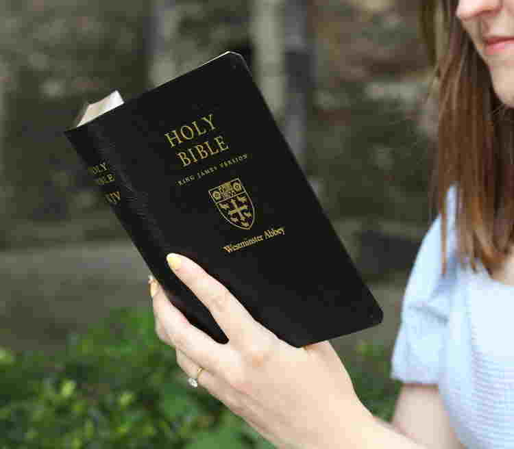 A woman holding a black leather bible with the Westminster Abbey Crest on