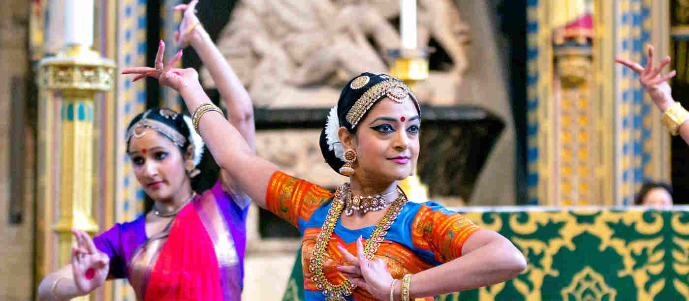 Photograph of women in brightly decorated clothing dancing as part of Commonwealth celebrations within the nave of Westminster Abbey
