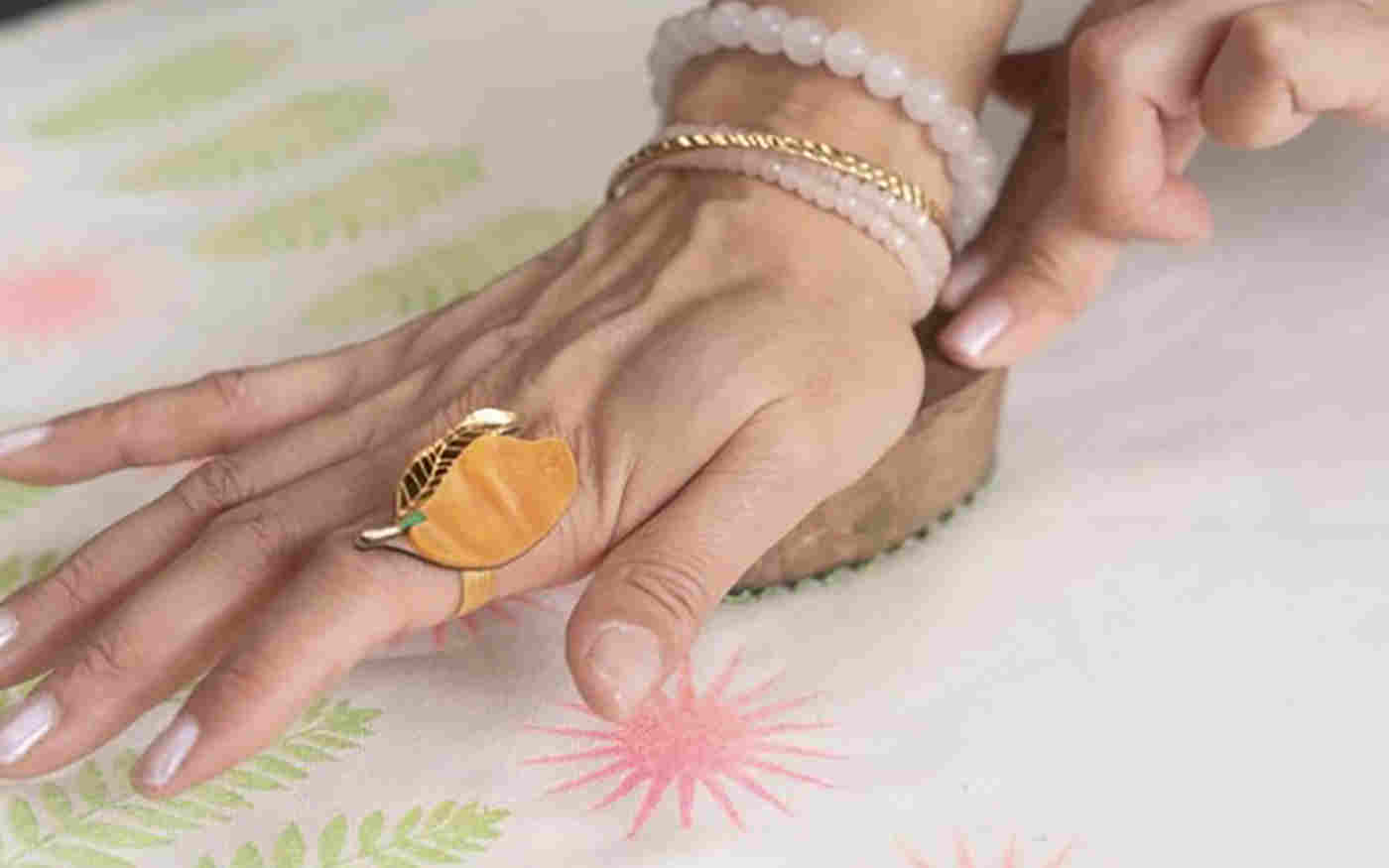 Photograph of a hand pressing down during a block printing workshop where there are green leaves being printed underneath