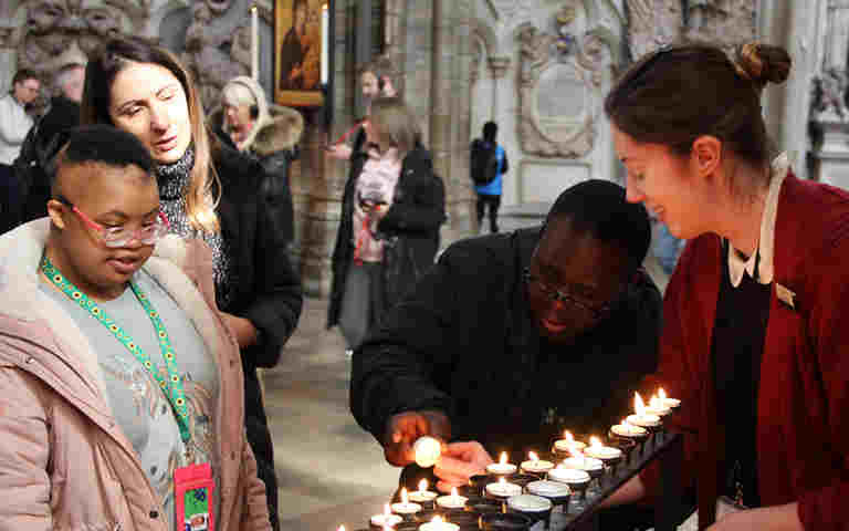 Photograph of young people and a member of staff votive lighting candles within the nave at Westminster Abbey