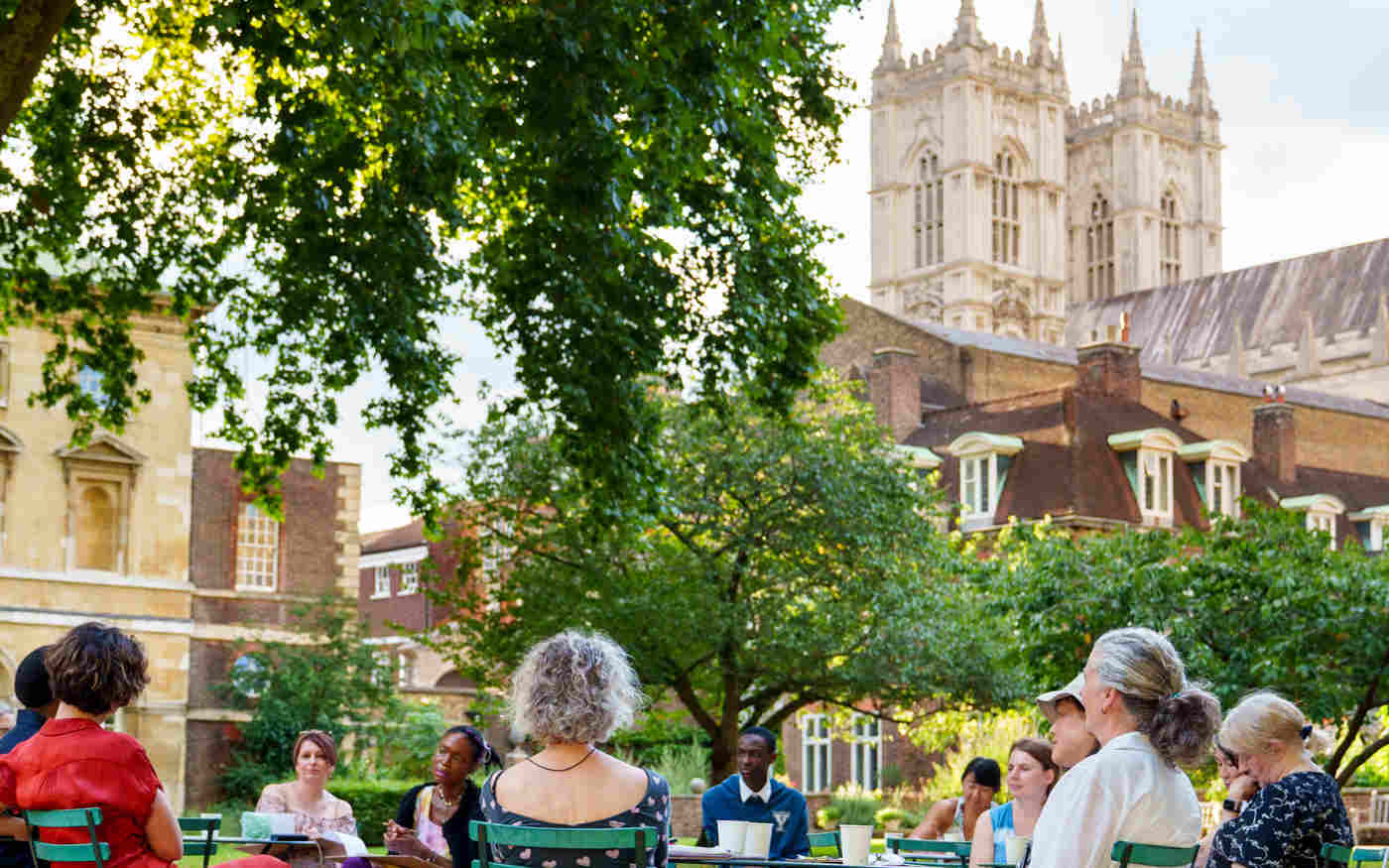 Photograph of visitors seated on chairs within College Garden, with the background of Westminster Abbey's West Towers