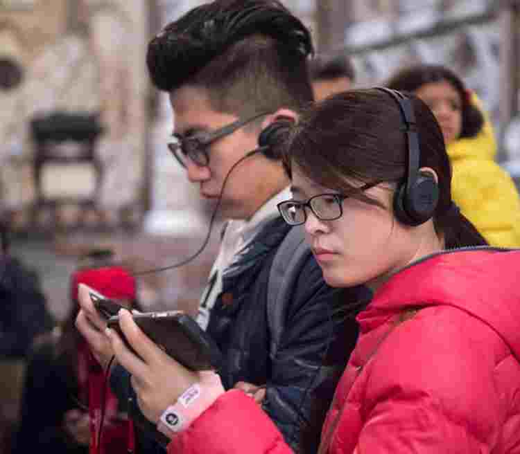 Two tourist visitors using Westminster Abbey's multimedia guide on smartphones and listening to the commentary with headphones