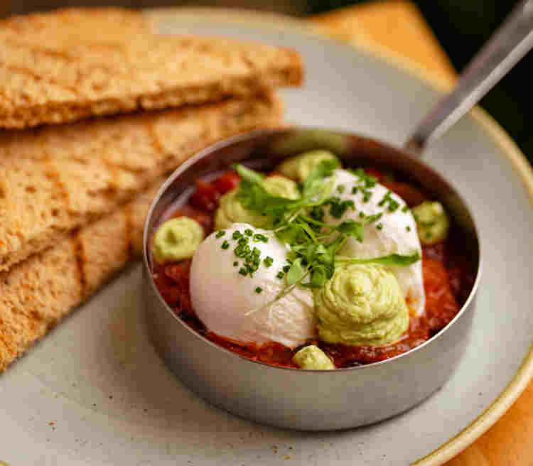 Poached eggs with smashed avocado in a red salsa next to toast