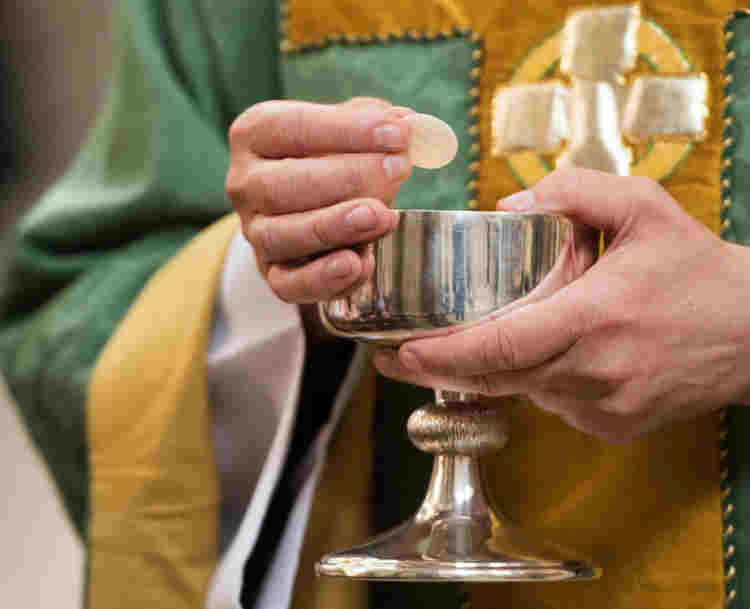 Close-up photograph of the cup, bread and hands of the priest during the Eucharist service, representing a Westminster Abbey lesson on the Eucharist for KS2
