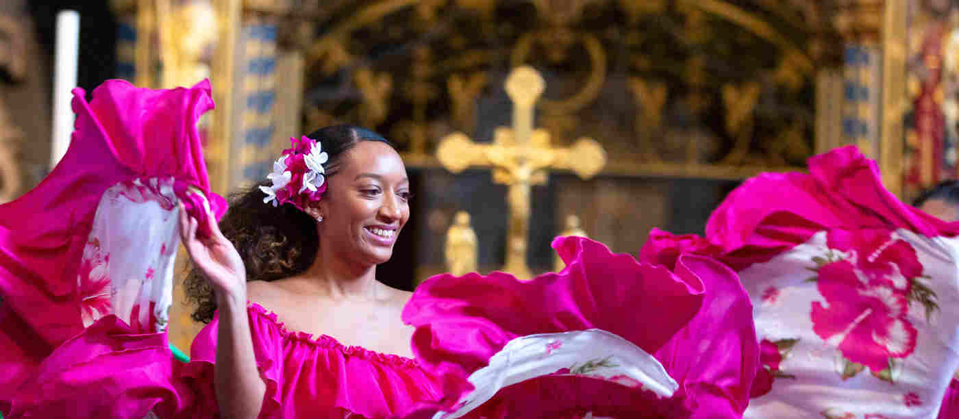 A smiling woman in a pink dress in front of an Altar